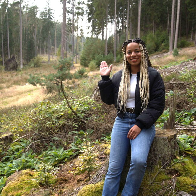 Auf dem Bild ist die Klimareporterin Alisha, im Wald an einen Baum gelehnt, zu erkennen.