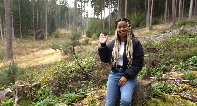 Auf dem Bild ist die Klimareporterin Alisha, im Wald an einen Baum gelehnt, zu erkennen.